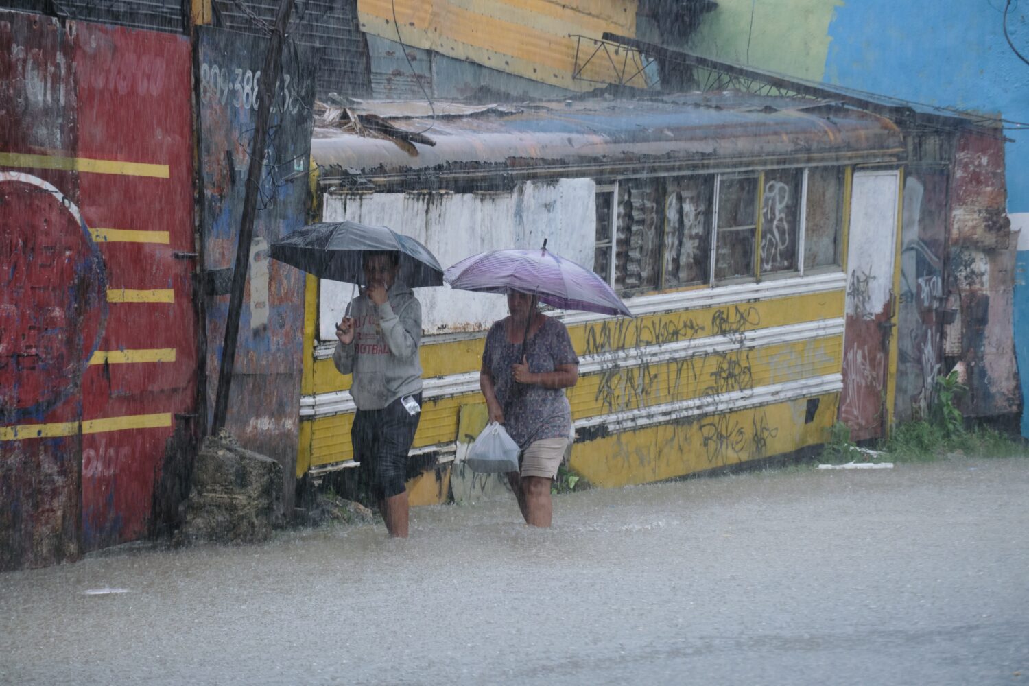 People wade through a street flooded by rains caused by Tropical Storm Melissa in Santo Domingo, Do...