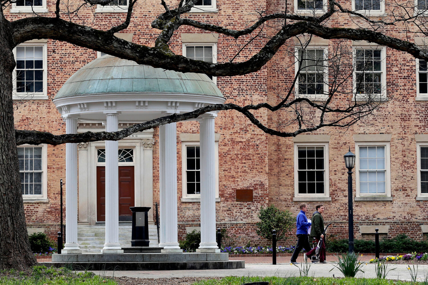 FILE - People walk through University of North Carolina campus March 18, 2020, in Chapel Hill, N.C....